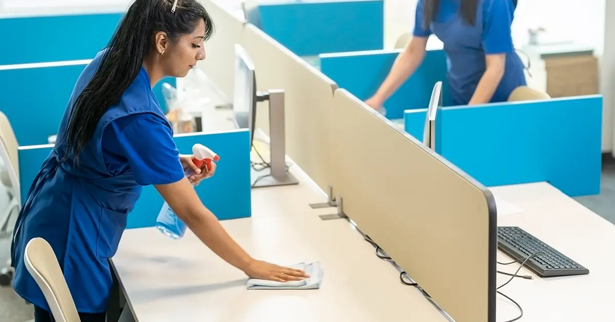 Cleaning ladies clean desks in an empty office space.